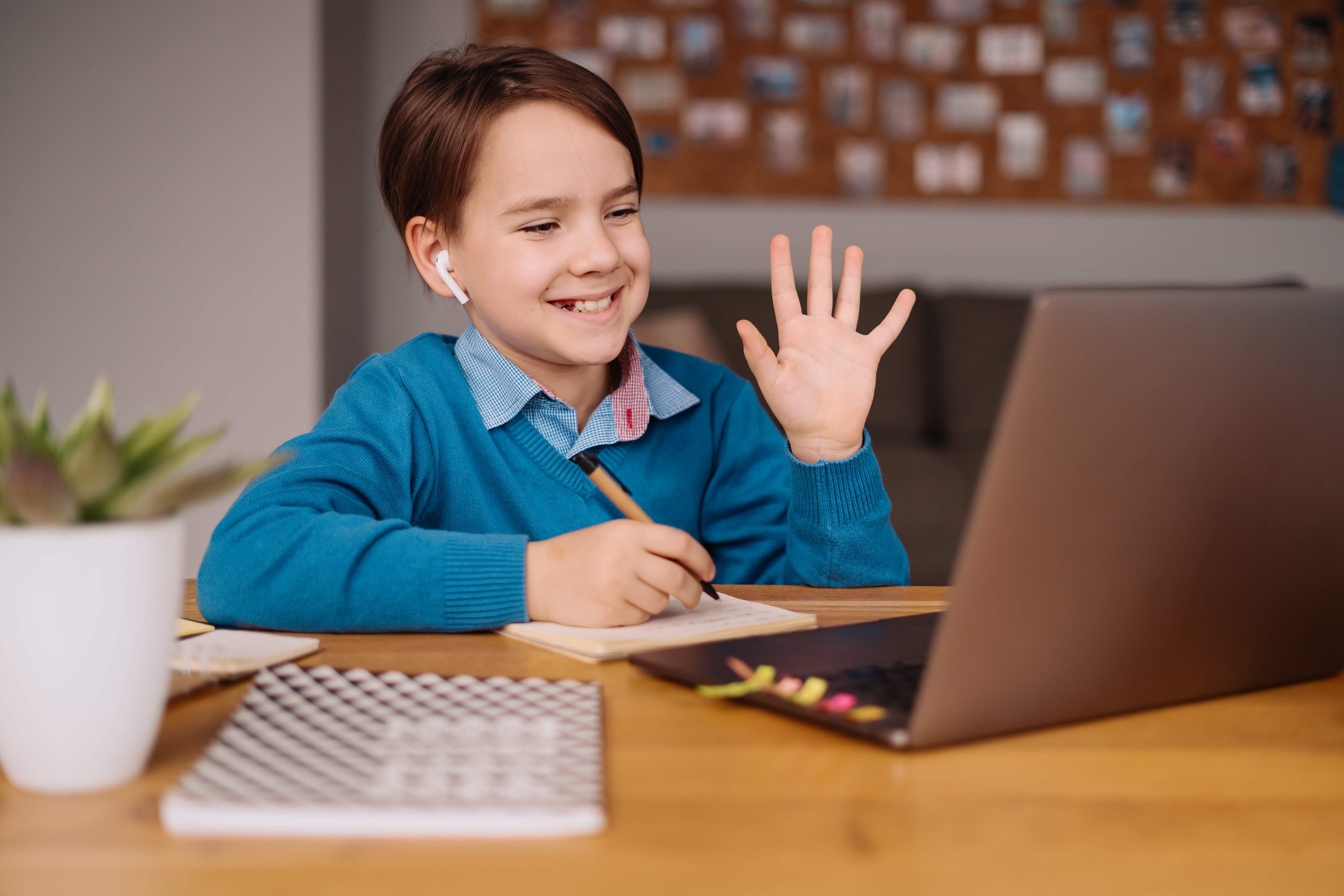 Boy learning online with laptop, waving at teacher