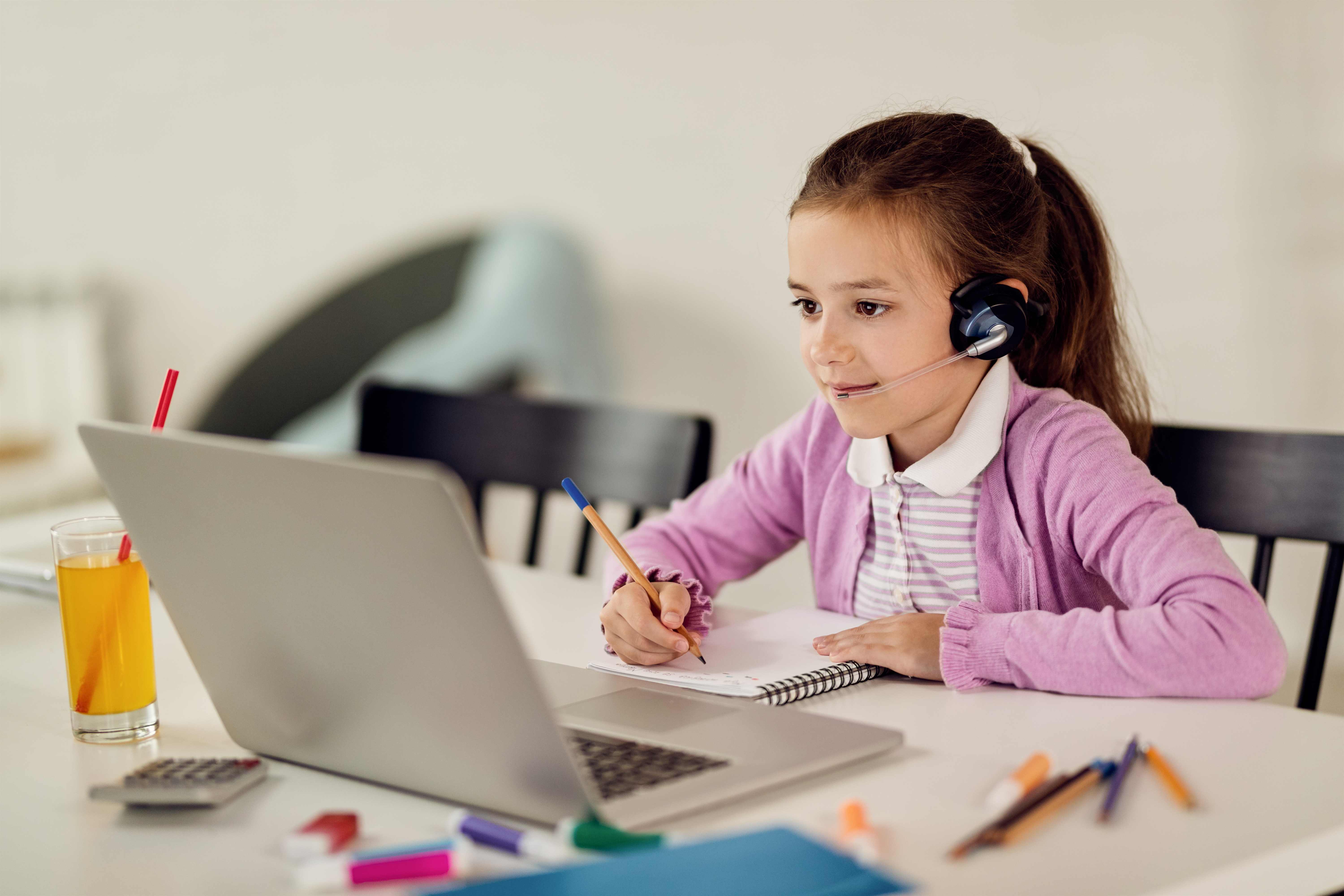 Girl writing notes while e-learning on laptop at home